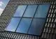 Solar-Flachkollektor von Vaillant, montiert auf einem geneigten Dach, mit vier vertikalen und zwei horizontalen Rahmen, reflektiert blaues Licht in den Himmel.